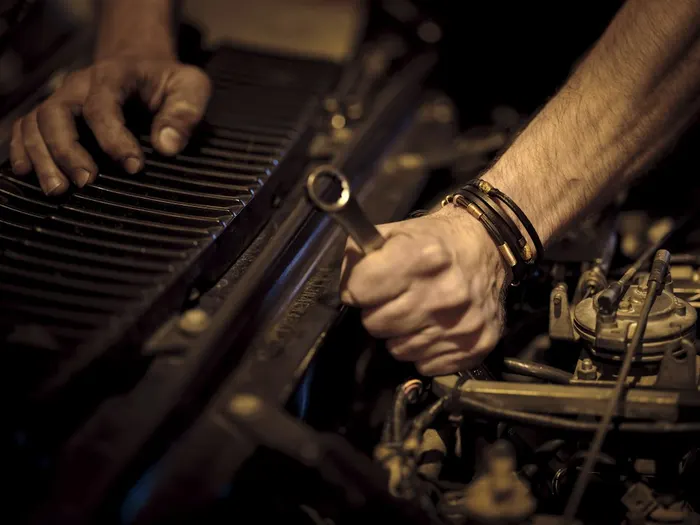 Manos de un mecánico ajustando una pieza del motor con una llave. Imagen de referencia.